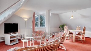 Quarto com televisão, cadeiras de vime, mesa de jantar e luminária no teto.