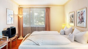 Hotellihuone, jossa on kaksi sänkyä, televisio, työpöytä ja ikkuna, jossa on verhot.