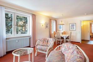 Een kamer met een eettafel, stoelen, een bank, een glazen bijzettafeltje en een radiator.