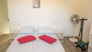 Un dormitori amb dos llits, vetustats blanques, un ventilador de peu i una cinta d'entrenament.