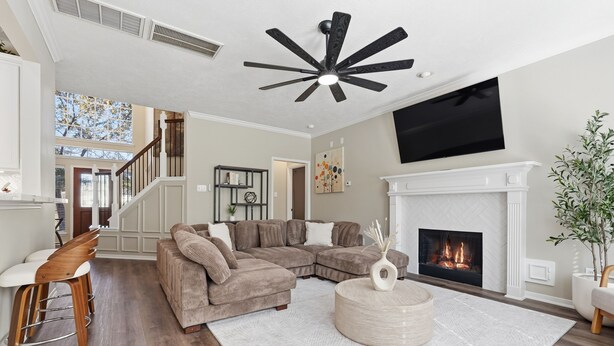 Ein Wohnzimmer mit Ecksofa, Kamin, Deckenventilator und einer Treppe zu einer oberen Ebene.