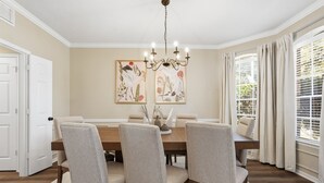 Ein Esszimmer mit einem Holztisch, vier Stühlen, einer Chandelierleuchtre und zwei gerahmten Pflanzenprints an der Wand.