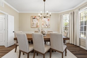 Ein Esszimmer mit einem Holztisch, vier Stühlen, einer Chandelierleuchtre und zwei gerahmten Pflanzenprints an der Wand.