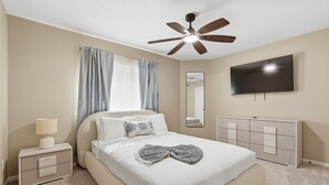 Ein Schlafzimmer mit Bett, Nachttisch, Lampe, Deckenventilator, Fernseher und Kleiderschrank.