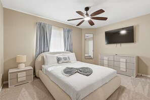 Ein Schlafzimmer mit Bett, Nachttisch, Lampe, Deckenventilator, Fernseher und Kleiderschrank.
