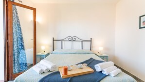 Ein ordentlich bezogenes Bett mit einer blauen, gemusterten Tagesdecke, ein Holztablett mit Handtüchern und einer Kerze sowie zwei Nachttische mit Lampen.