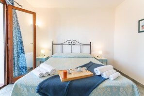 Un lit bien fait, recouvert d’une couvre-lit bleue à motifs, un plateau en bois avec des serviettes et une bougie, et deux tables de chevet avec des lampes.