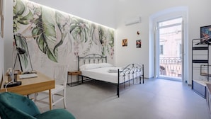 A bedroom with a bed, a desk, a chair, a large floral wall mural, a balcony with a railing, and a door leading outside. - GuestHost - Charming 74 sqm apartment, ideal for groups or families of up to 4 guests, located on the first floor of a building (a few steps to access / NO elevator).The accommodation is located in a very central area, just a few minutes’ walk from the (Taranto)