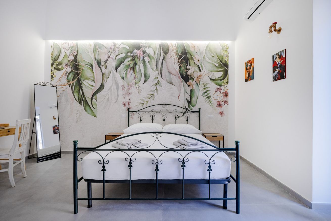 Un dormitorio con cama, mesita de noche, silla y pared decorada con un mural floral.