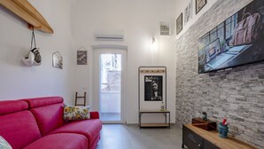 A living room with a red sofa, a stone wall, a television, and a door leading outside. - GuestHost - Charming 74 sqm apartment, ideal for groups or families of up to 4 guests, located on the first floor of a building (a few steps to access / NO elevator).The accommodation is located in a very central area, just a few minutes’ walk from the (Taranto)