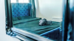 A neatly made bed with a tufted headboard, a green bedspread, and a folded towel on the side.