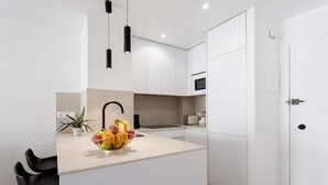 Una cucina moderna con mobili bianchi, un'isola centrale con una ciotola di frutta, lampade a sospensione nere e un forno a microonde.