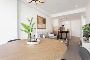 A modern living space with a round wooden dining table, a sofa set, a kitchen area, and a large plant. - Genteel Home Pedro Teixeira (Madrid)