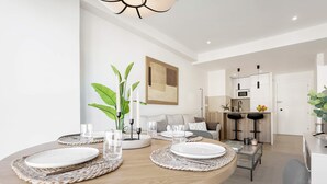Un'elegante zona pranzo con un tavolo rotondo apparecchiato per quattro, una cucina sullo sfondo e un soggiorno con divano e sgabelli da bar.