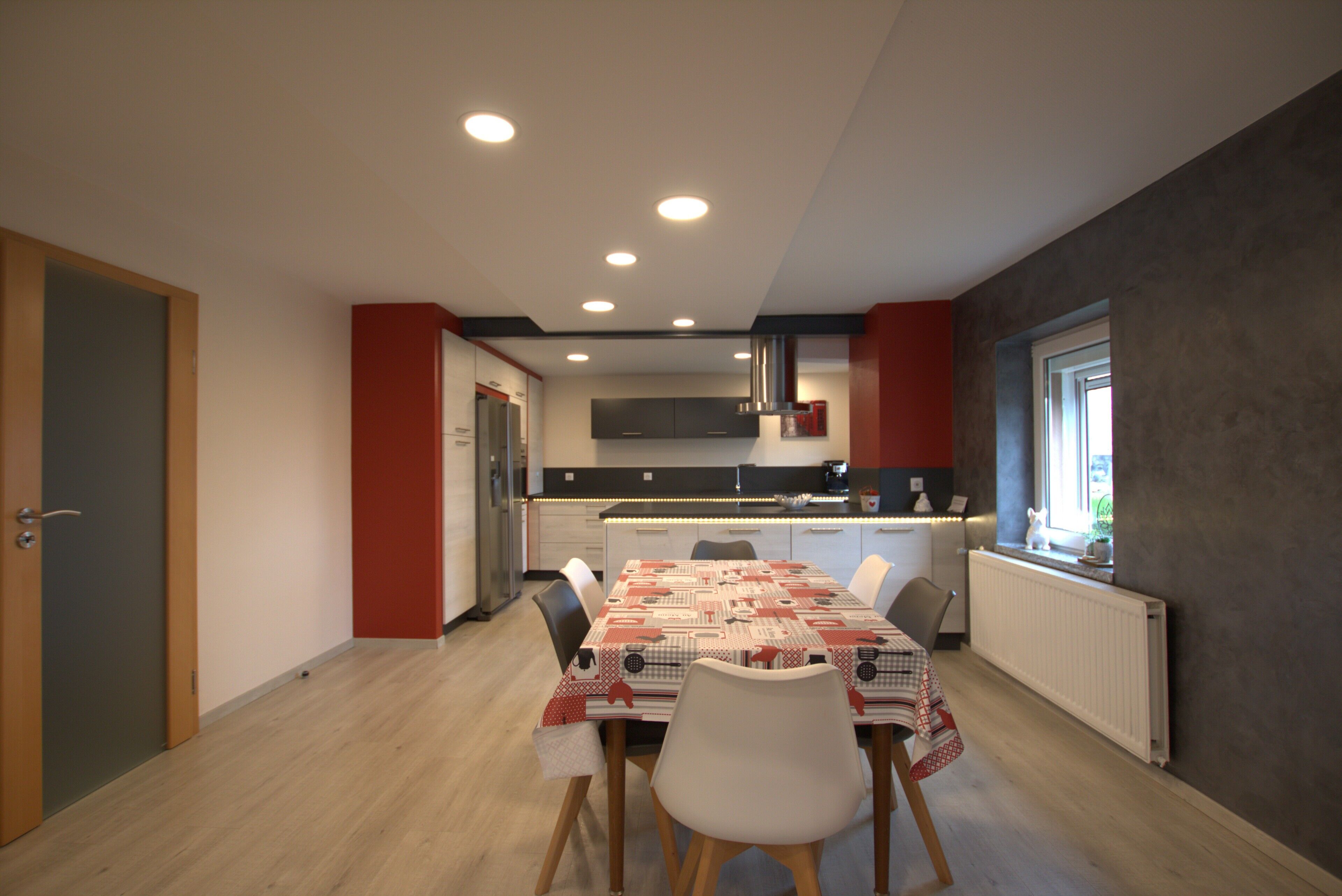 A modern kitchen with a central island, white cabinets, and a red accent wall.