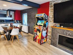 A modern living room with a dining area, a fireplace, and a large flat-screen TV. - Au Jardin Du Levant" gîte with large swimming pool and games room (Holving)