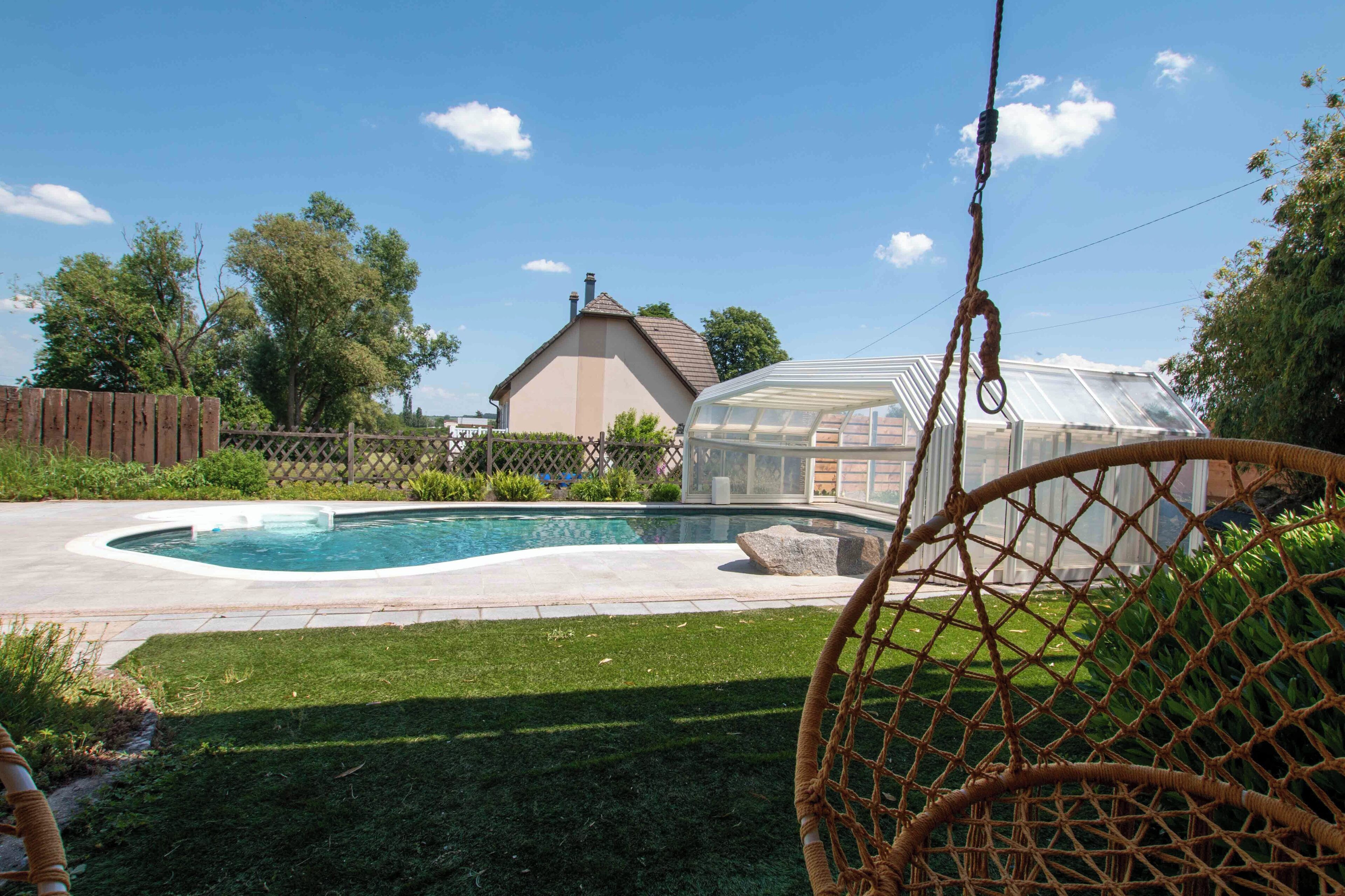 Um quintal com piscina, estufa e cerca de madeira.