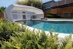 A swimming pool with a glass-enclosed structure, surrounded by ferns. - Au Jardin Du Levant" gîte with large swimming pool and games room (Holving)