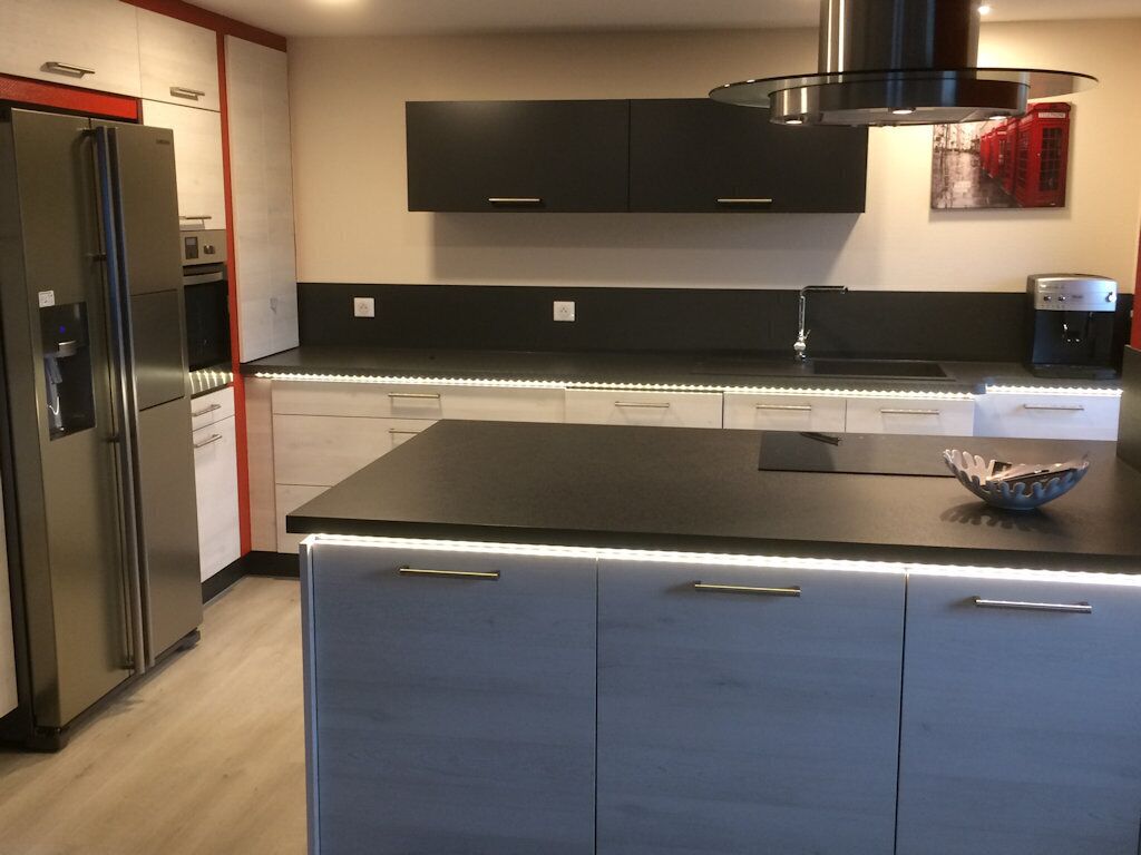 A modern kitchen with a stainless steel refrigerator, black cabinets, a black countertop, and a built-in oven.
