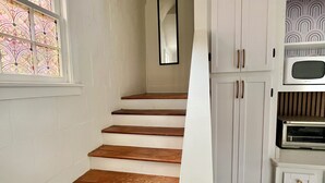 A staircase with wooden steps leading to a landing, a white wall, and a kitchen area with cabinets and appliances.