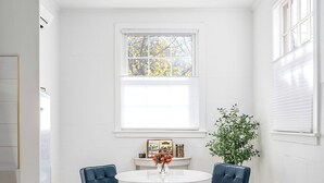 A dining area with a round table, two chairs, a patterned rug, and a window with a view of trees.