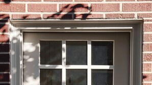 A white door with a window above it, a keypad lock, and a brick wall.