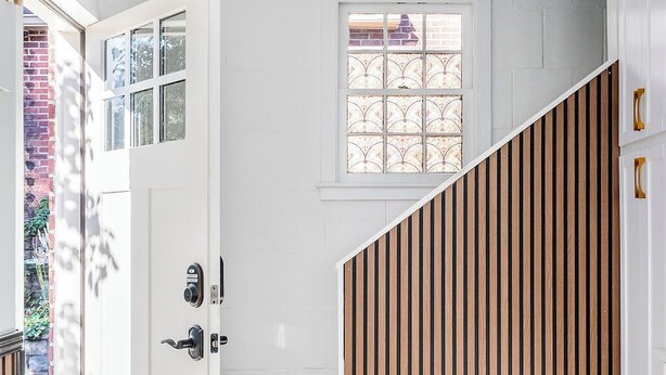A modern interior with a white door, a wooden slatted wall, and a small window with decorative glass.