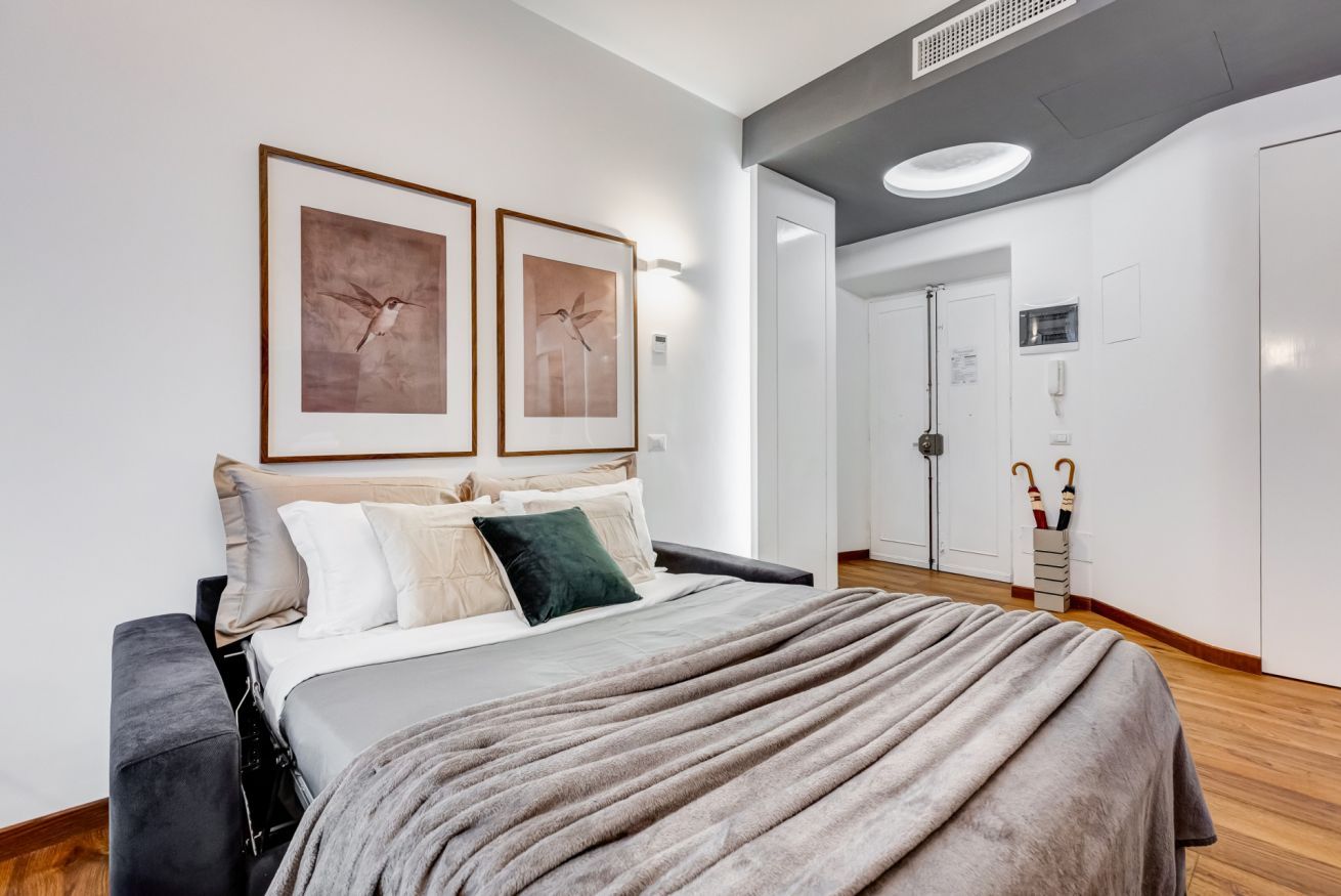 A modern bedroom with a bed, two framed artworks, a bedside table, and a wardrobe.