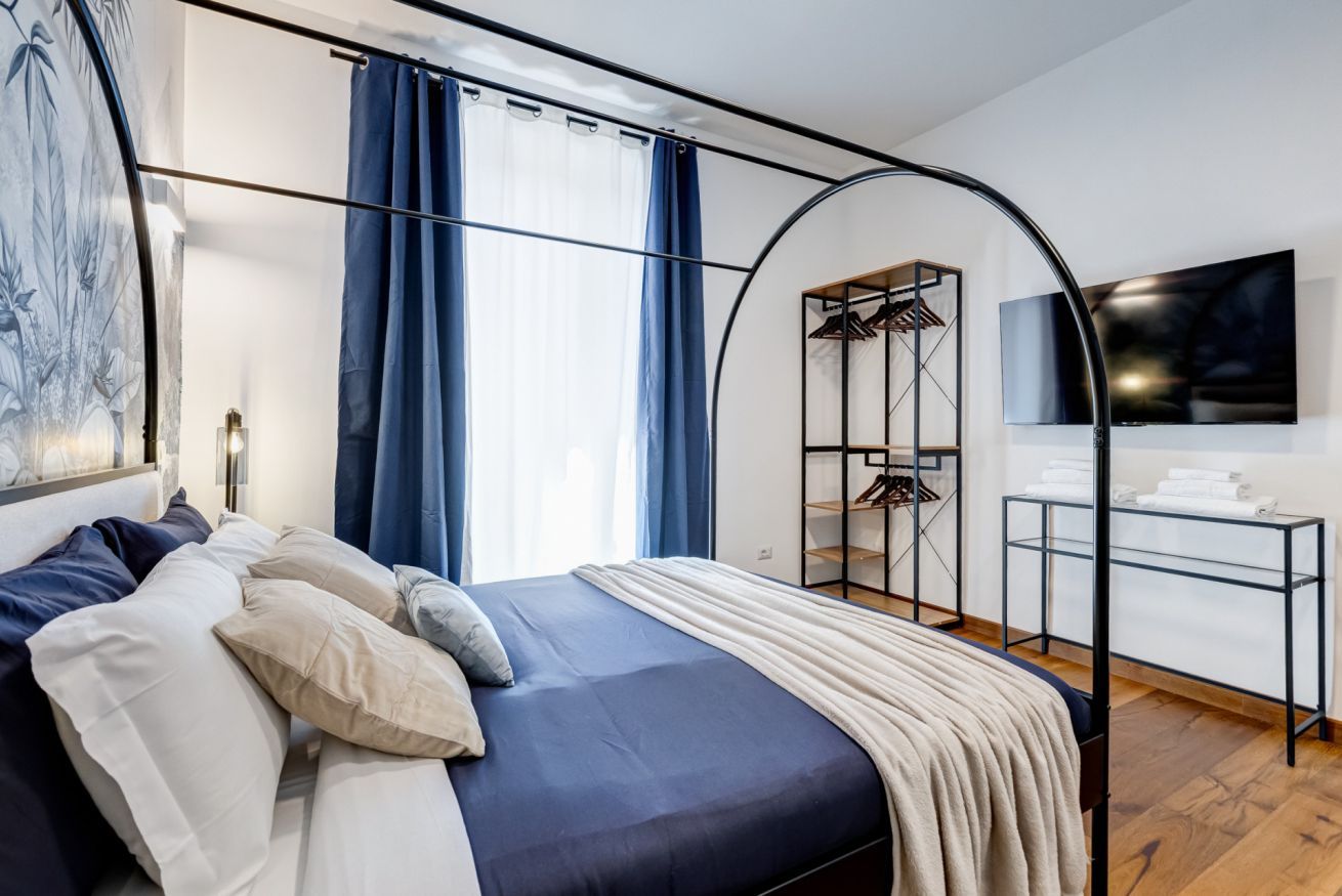 A modern bedroom with a bed, a wardrobe, a TV, and a window with curtains.
