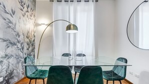 Un espace repas moderne avec une table en verre, quatre chaises vertes, un grand lampadaire et un rideau blanc.