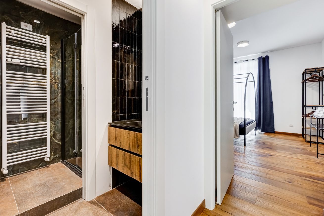 A modern interior with a kitchen, a wooden floor, and a glass door leading to a bathroom.