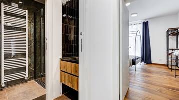 A modern interior with a kitchen, a wooden floor, and a glass door leading to a bathroom.