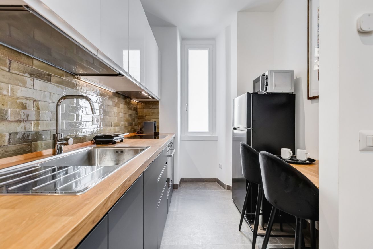 Una cocina moderna con encimera de madera, pileta de acero inoxidable y sillas negras en una mesa de comedor.