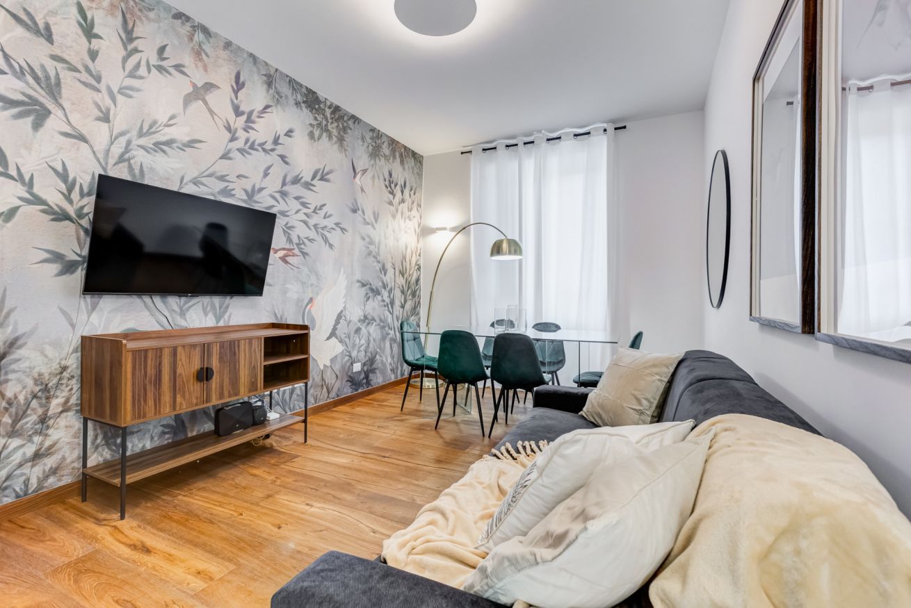 A modern living room with a TV, wooden cabinet, sofa, and a dining area with chairs.