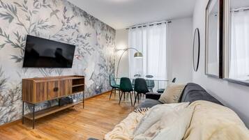 Una sala moderna con televisor, mueble de madera, sofá y comedor con sillas.