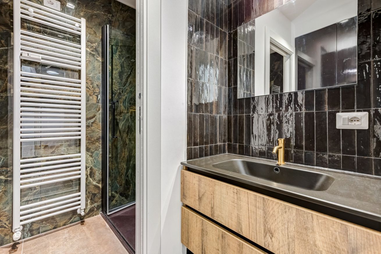 A bathroom with a marble wall, a white towel rack, a sink with a gold faucet, and a mirror.