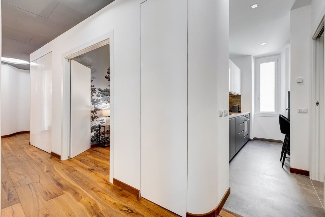 A modern interior with a wooden floor, white walls, and a kitchen area with grey cabinets and a black chair.