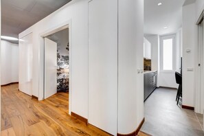 A modern interior with a wooden floor, white walls, and a kitchen area with grey cabinets and a black chair. - BDC - Dragonfly 3BDR 2BATH @Testaccio (roma)