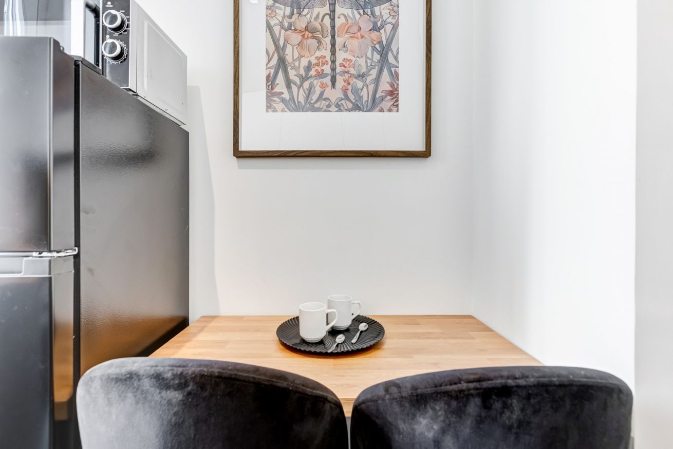 Una cocina moderna con refrigerador, una mesa de madera y dos sillas, y una obra de arte floral enmarcada en la pared.