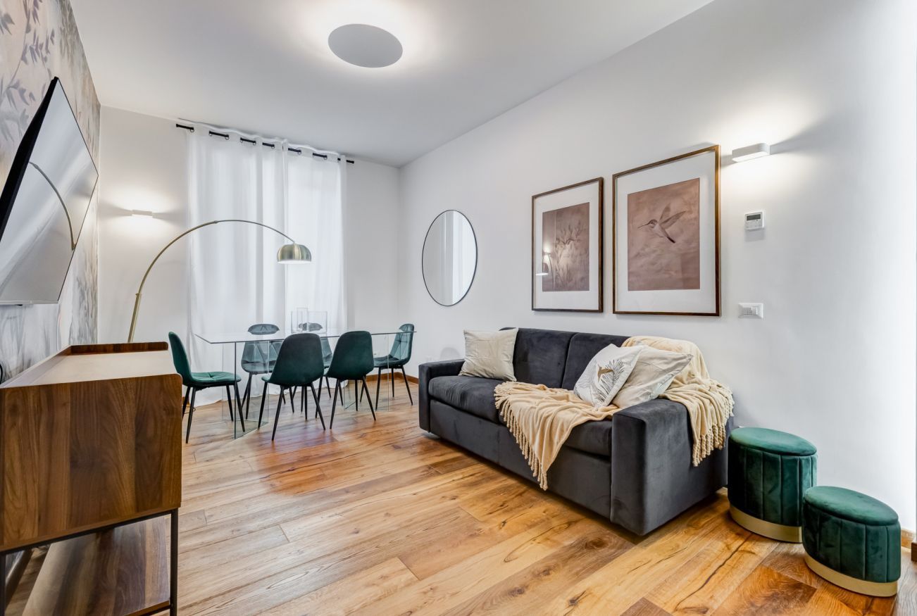 A modern living room with a sofa, a dining table with chairs, a mirror, and artwork on the walls.