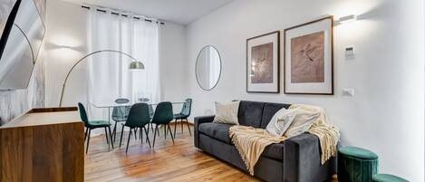 A modern living room with a sofa, a dining table with chairs, a mirror, and artwork on the walls.