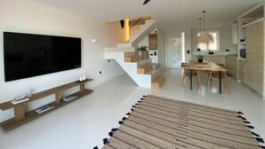 Un saló modern amb televisió de pantalla plana, un moble de roba per a l'entreteniment i una escala que condueix a una zona de cuina.