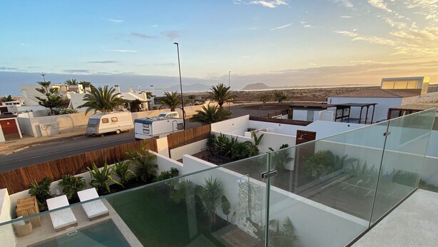 Zona de piscina al terrat amb baranes de vidre, gandules i vistes del paisatge circumdant.