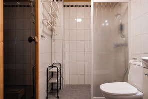 A bathroom with a shower, toilet, and a metal rack with shelves. - Alpine Cottage by Aavalevi (Levi)