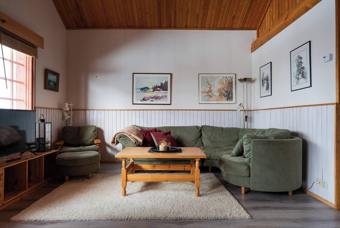 Un salon chaleureux avec un plafond en bois, un canapé vert, une table basse en bois et des tableaux encadrés accrochés aux murs.