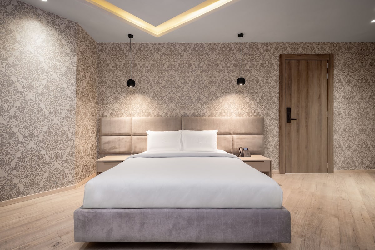 A modern bedroom with a large bed, two bedside tables, a wooden door, and patterned wallpaper.