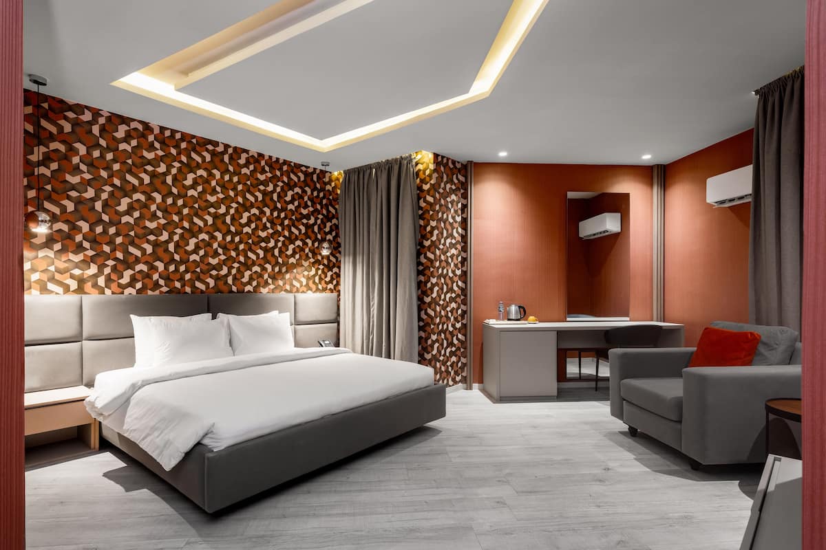 A modern hotel room with a large bed, a desk, and a seating area.