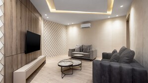 A modern living room with a flat-screen TV, grey sofa, and two round coffee tables. - Atlanticblu Hotels & Resorts (Abuja)