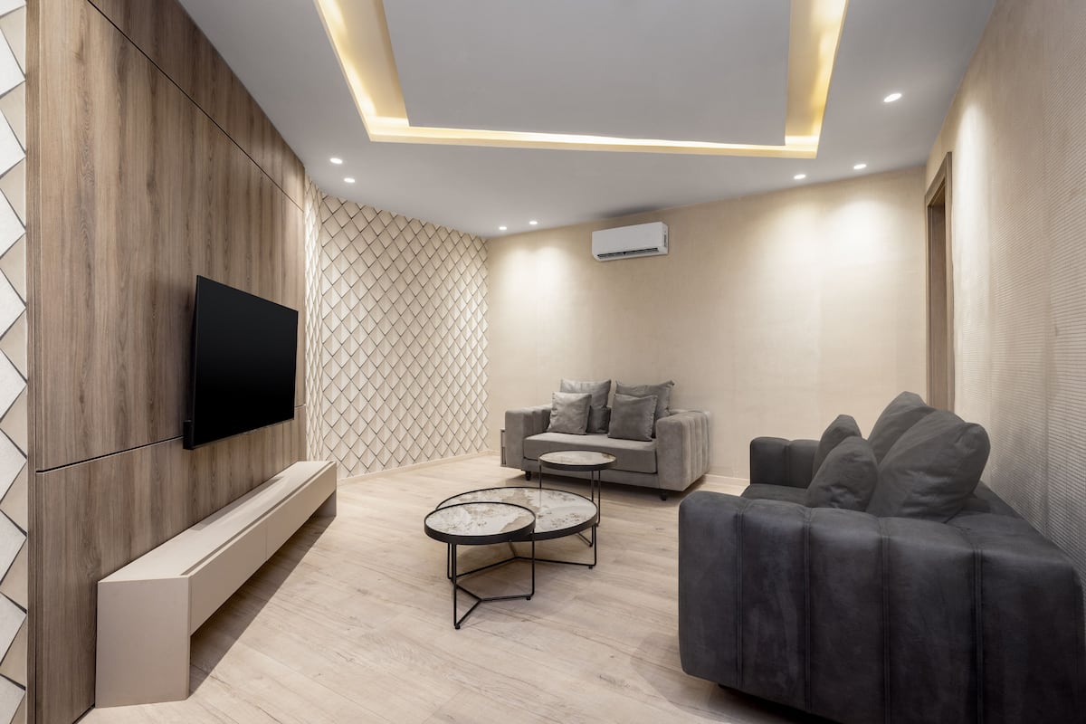 A modern living room with a flat-screen TV, grey sofa, and two round coffee tables.