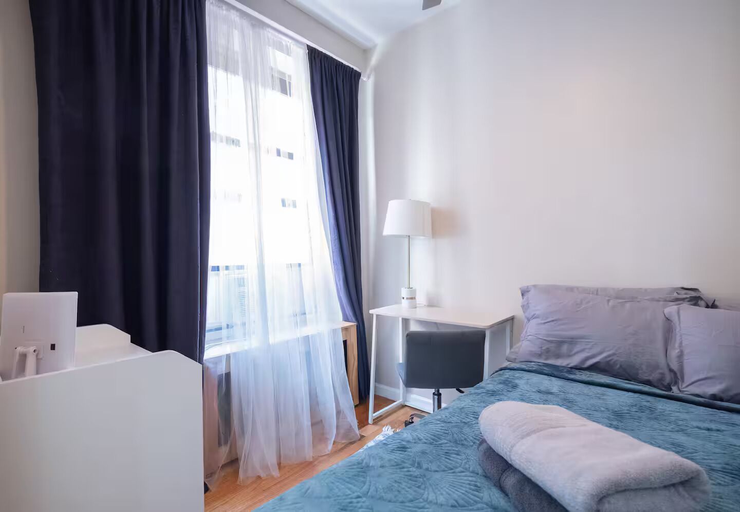 Une chambre d’hôtel avec un lit, un bureau, une lampe et une fenêtre avec des rideaux.